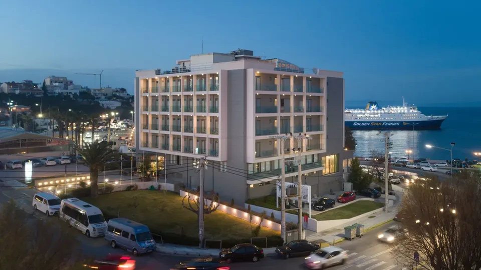 Hotel Avra lit up at dusk beside Rafina port, with a Golden Star ferry berthed behind it