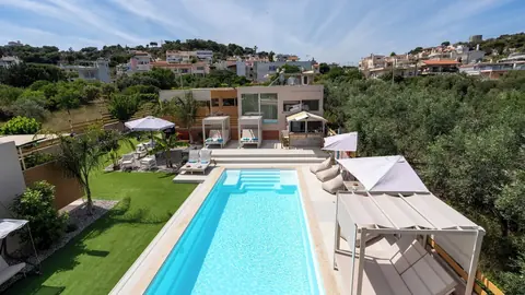 A private heated pool with sun loungers and shaded day beds outside a modern bungalow among olive trees