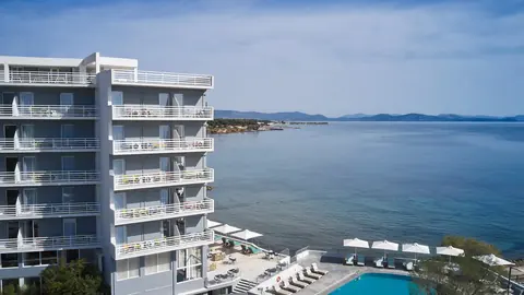 NLH Mati Seafront's balconies above a poolside terrace, with the bay and headland beyond